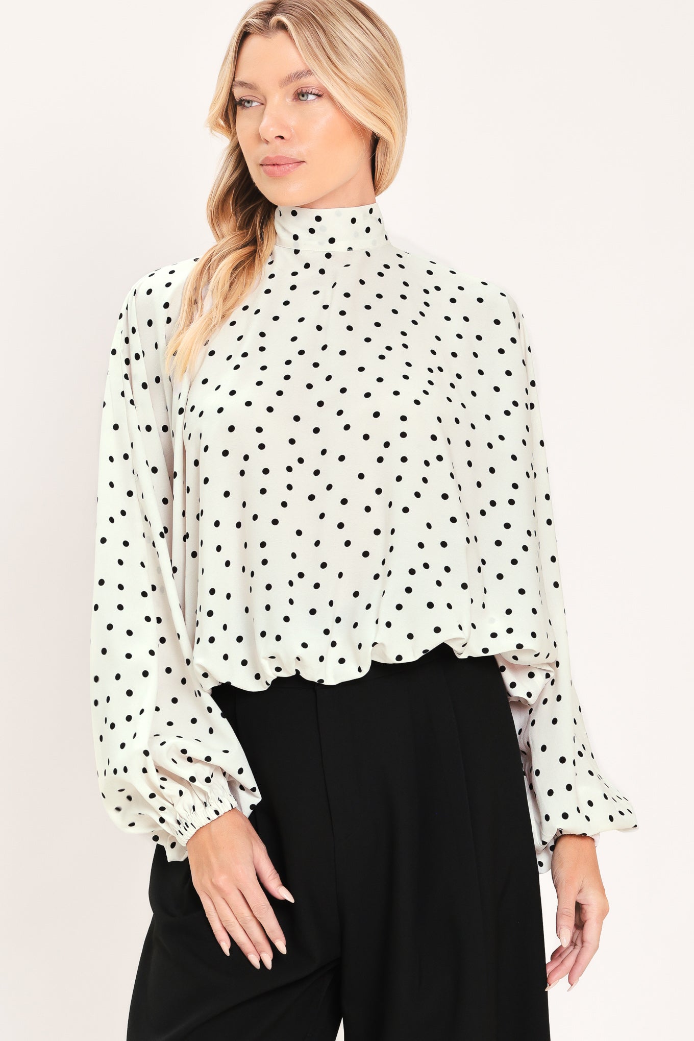 A woman wearing a white long-sleeve blouse with a black polka dot pattern and a high mock neck | Flying Tomato