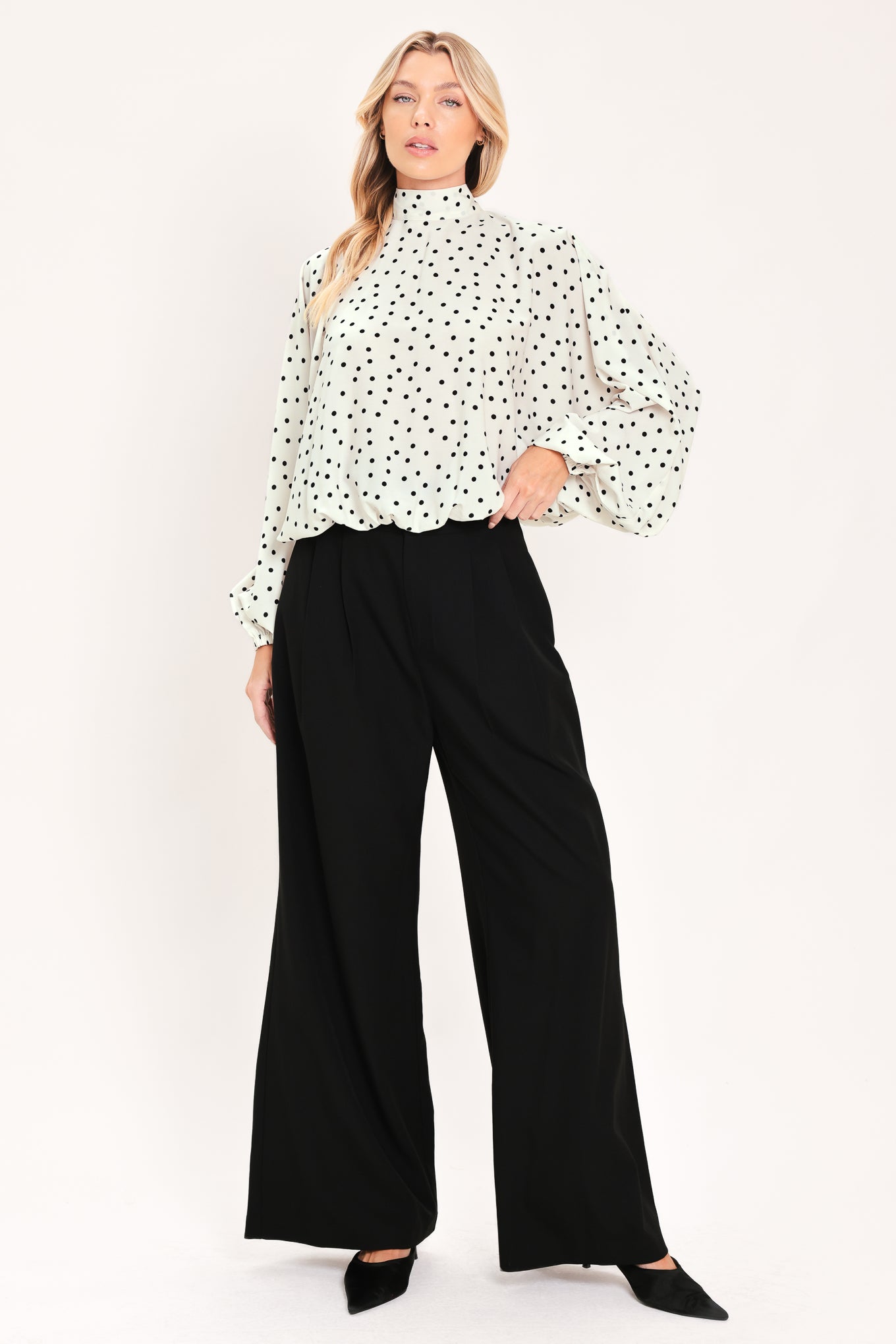 A woman wearing a white long-sleeve blouse with a black polka dot pattern and a high mock neck | Flying Tomato