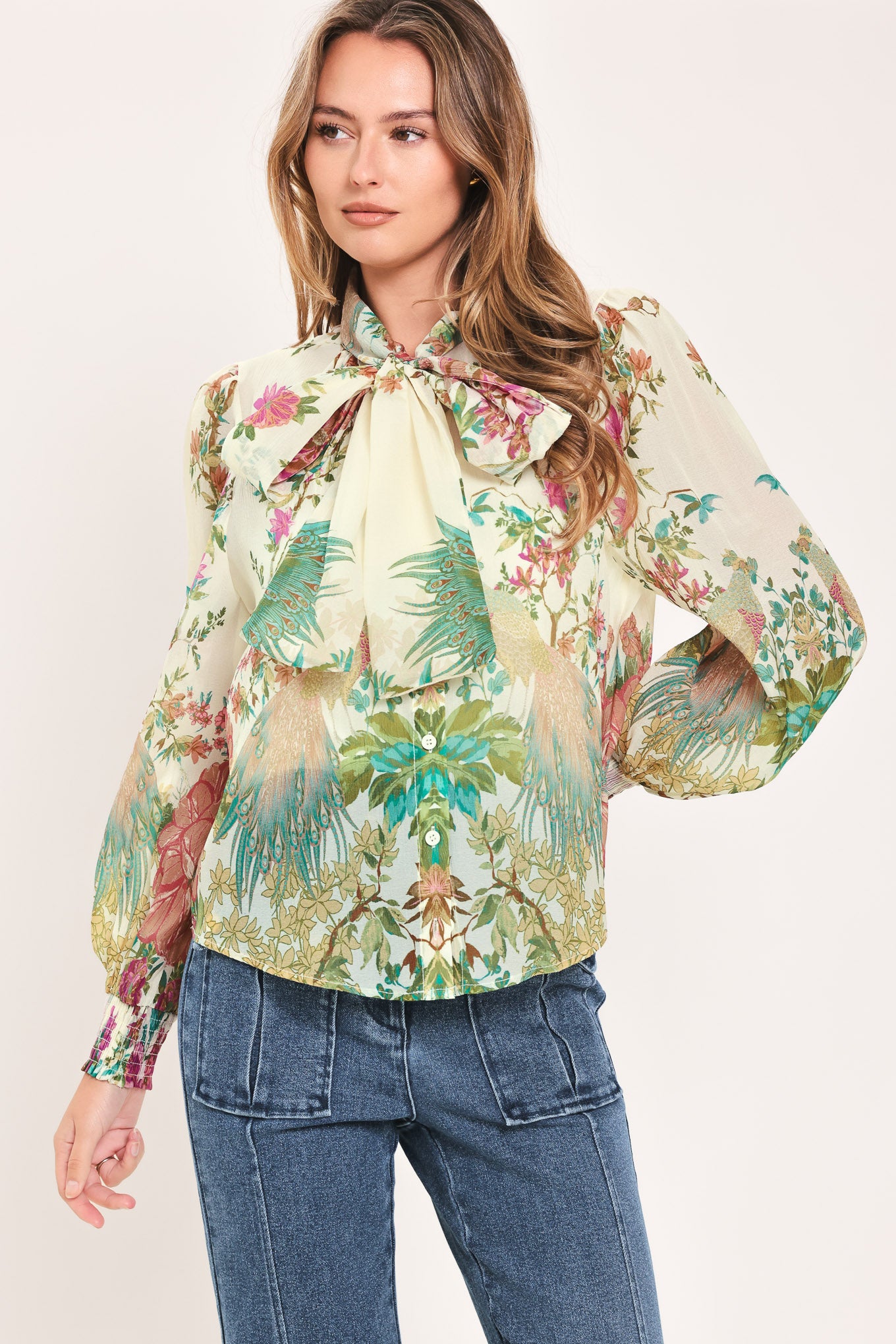 A woman wearing a long-sleeve blouse with a large bow at the collar and a tropical floral print | Flying Tomato