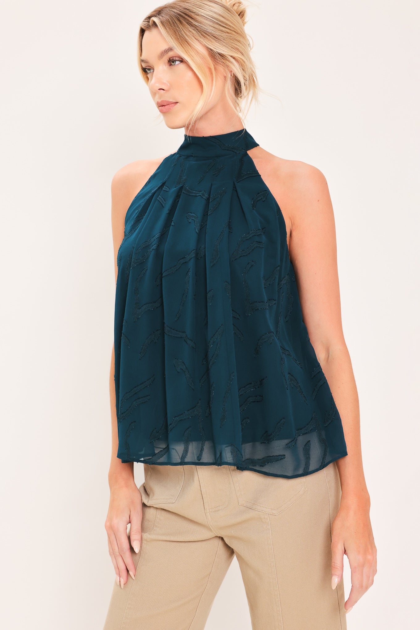 A woman wearing a sleeveless high-neck halter top in dark teal with a subtle tonal pattern | Flying Tomato