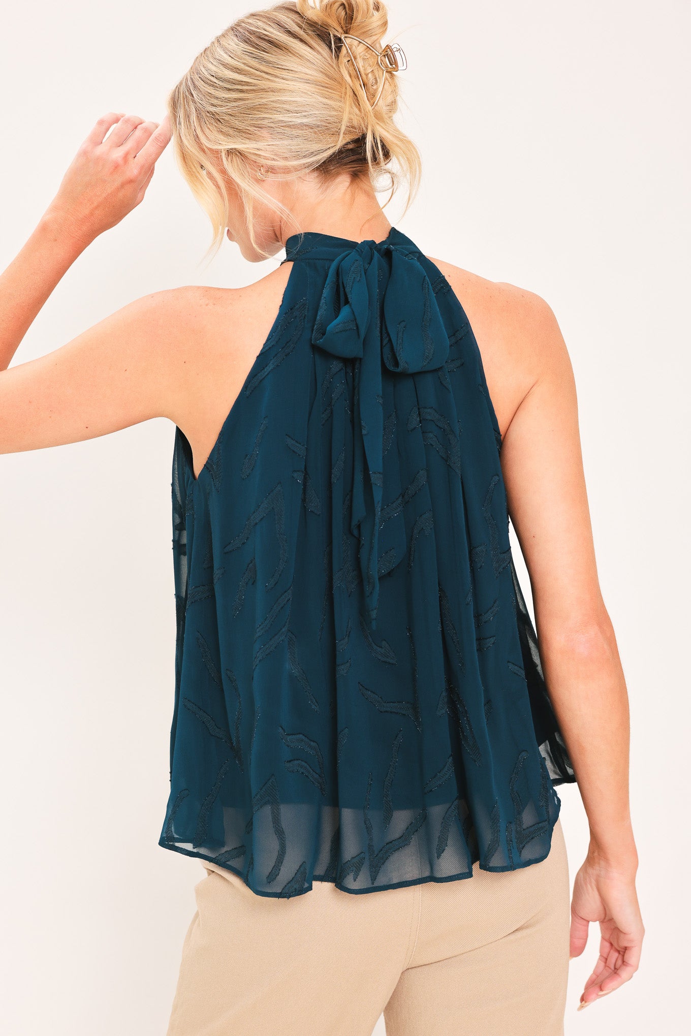 A woman wearing a sleeveless high-neck halter top in dark teal with a subtle tonal pattern | Flying Tomato