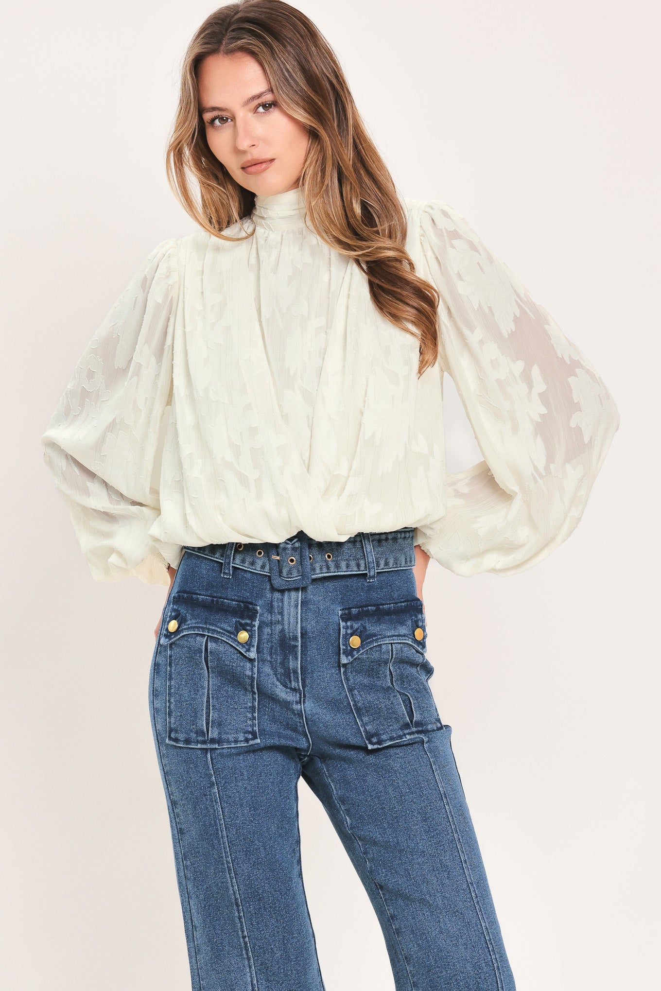 A woman wearing a cream-colored, semi-sheer long-sleeve blouse with a high neck | Flying Tomato