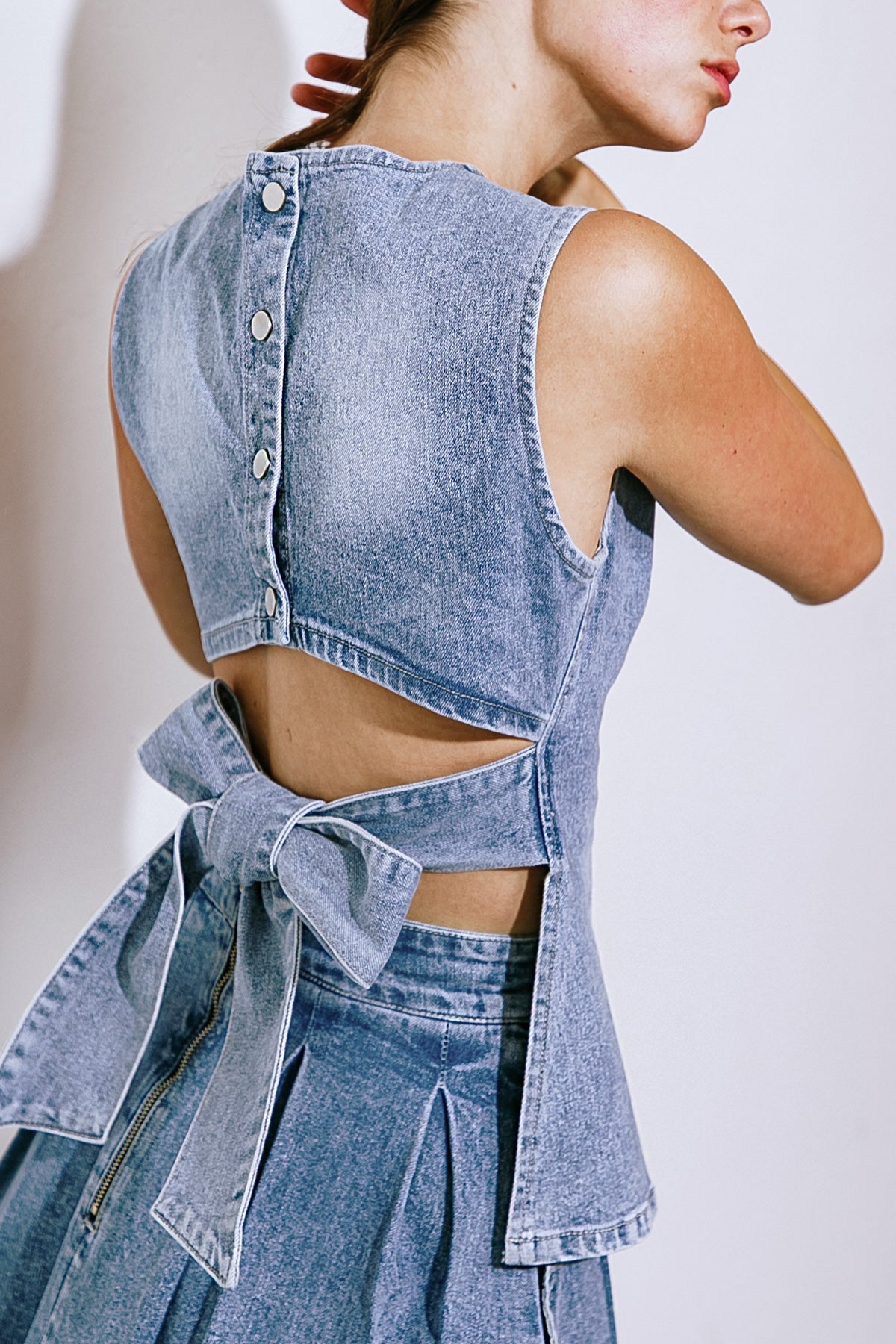 Experience exquisite style with our washed denim top, boasting a round neckline, sleeveless design, and back button down/tie closure.