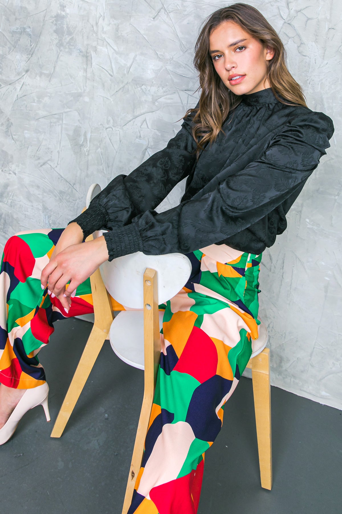 A satin top featuring high neckline, long puff sleeve with smocked cuff and back sash tie closure