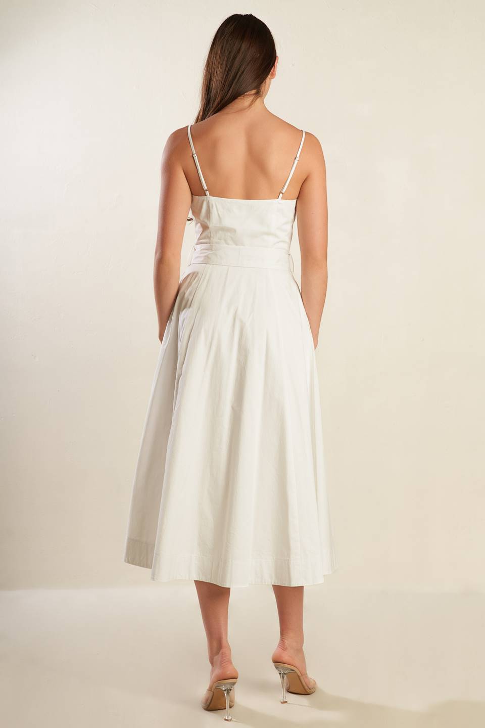 A solid white woven midi dress featuring straight neckline straps, button down, side pockets, self sash belt and full skirt.