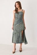 A woman modeling a sleeveless, mid-length denim dress with a distressed denim acid-wash finish, featuring a high side slit and brown pointed-toe heels | FREEMARKET