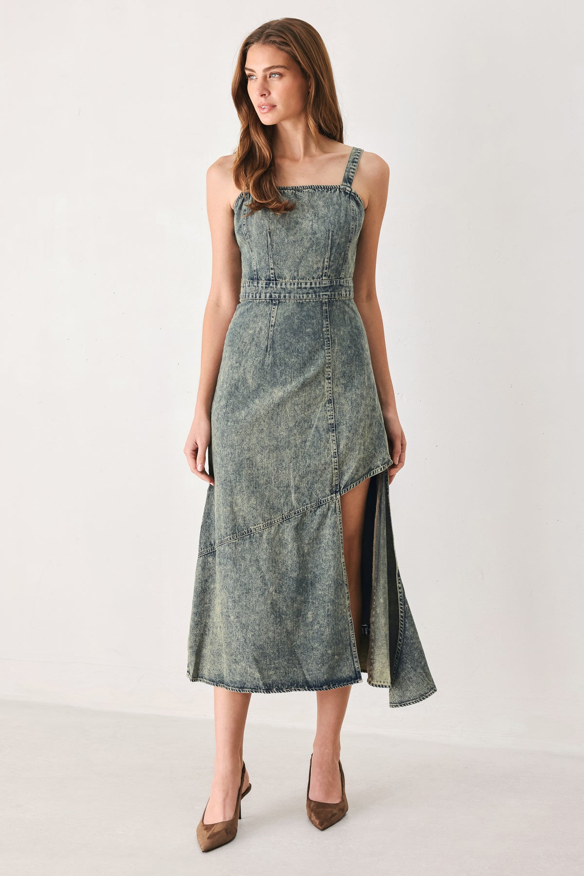 A woman modeling a sleeveless, mid-length denim dress with a distressed denim acid-wash finish, featuring a high side slit and brown pointed-toe heels | FREEMARKET