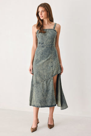 A woman modeling a sleeveless, mid-length denim dress with a distressed denim acid-wash finish, featuring a high side slit and brown pointed-toe heels | FREEMARKET