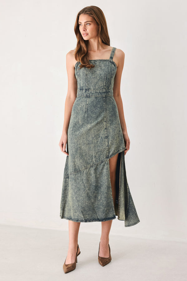 A woman modeling a sleeveless, mid-length denim dress with a distressed denim acid-wash finish, featuring a high side slit and brown pointed-toe heels | FREEMARKET