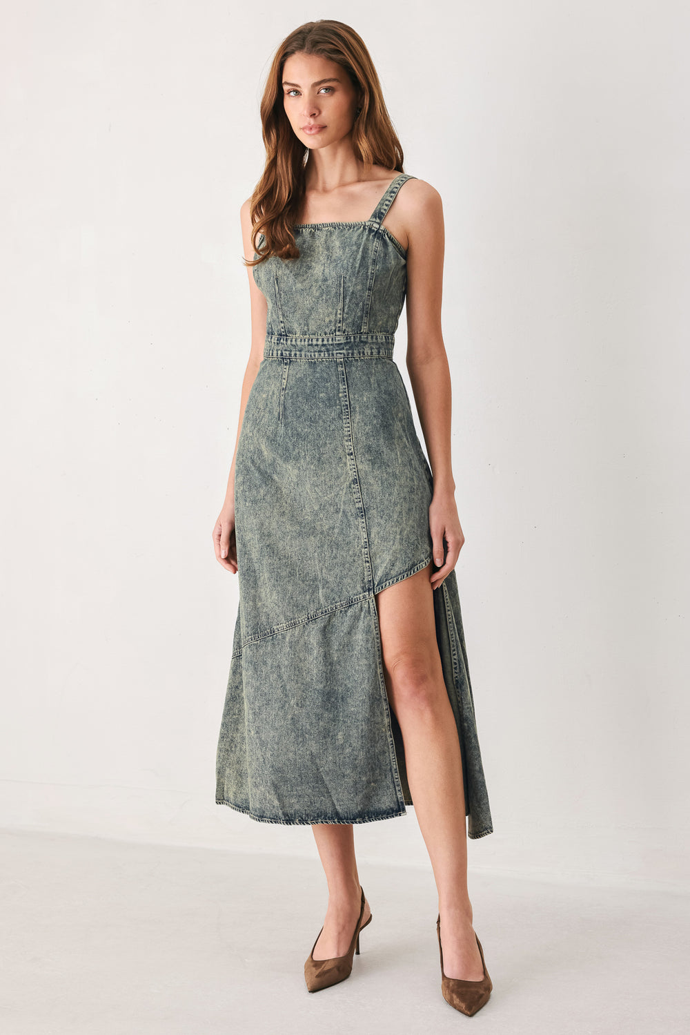 A woman modeling a sleeveless, mid-length denim dress with a distressed denim acid-wash finish, featuring a high side slit and brown pointed-toe heels | FREEMARKET