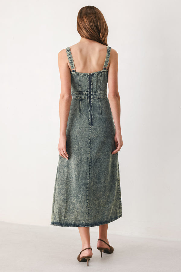 A woman modeling a sleeveless, mid-length denim dress with a distressed denim acid-wash finish, featuring a high side slit and brown pointed-toe heels | FREEMARKET