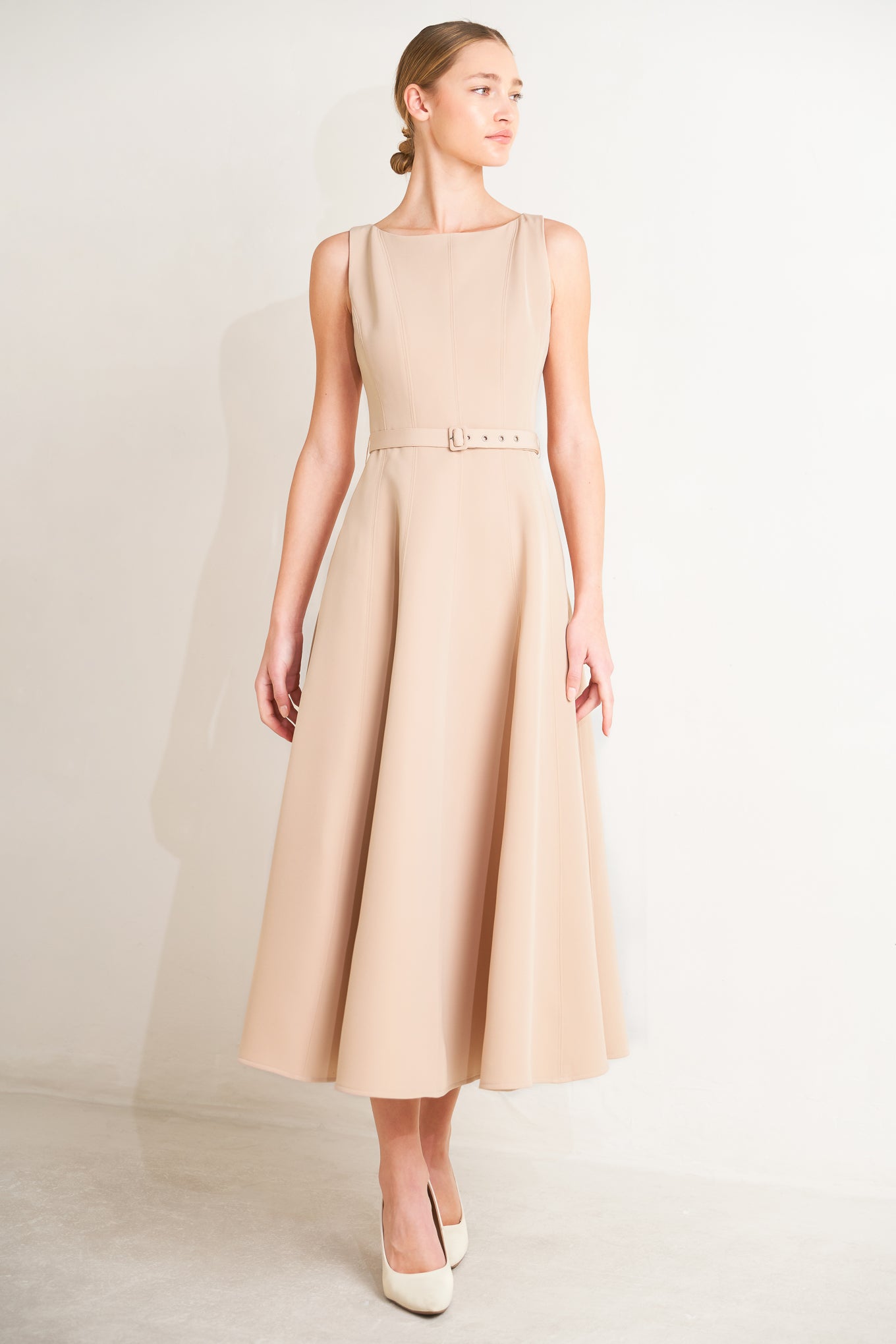Woman wearing a beige sleeveless dress with a belt on a white background