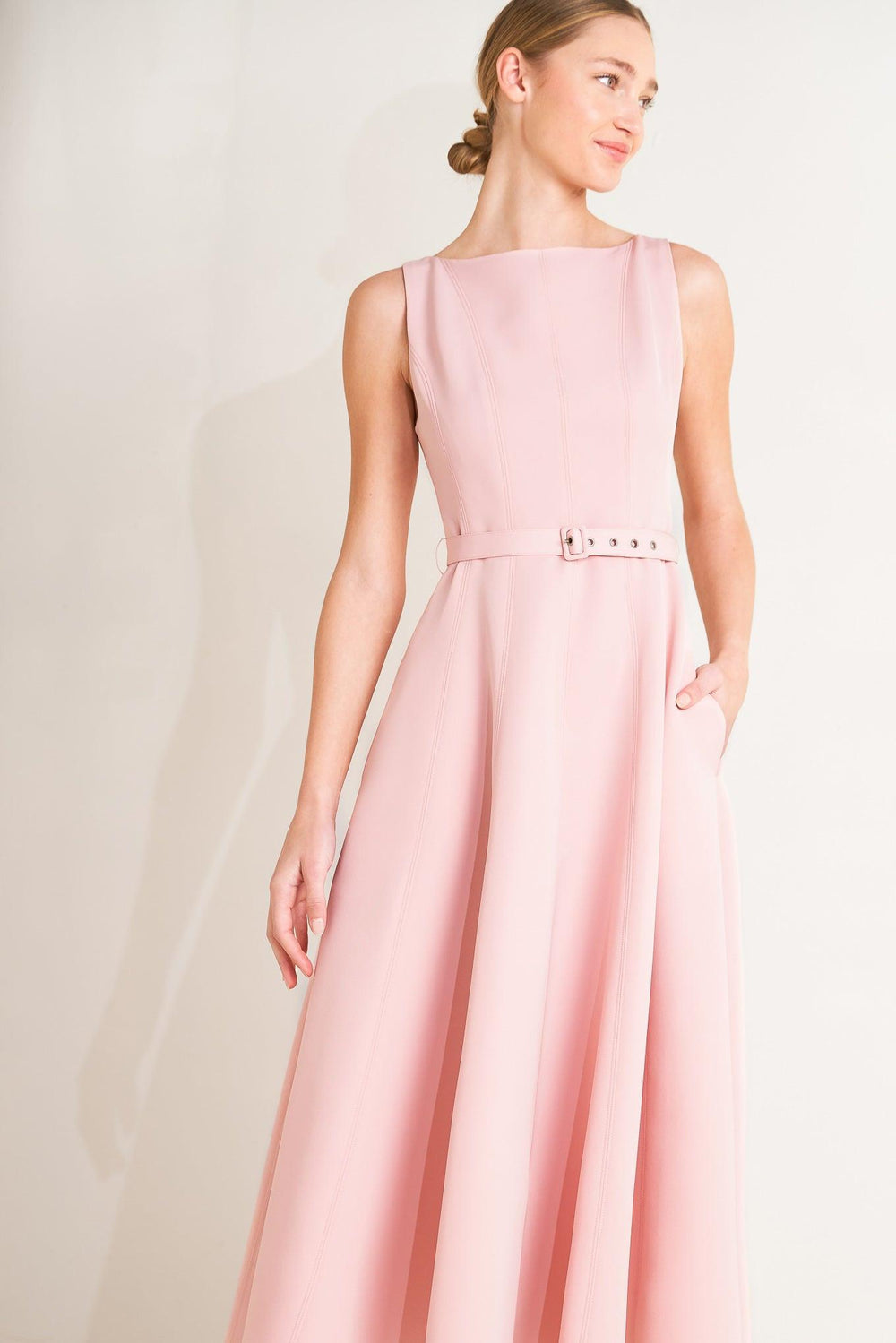 Woman wearing a beige sleeveless dress with a belt on a white background
