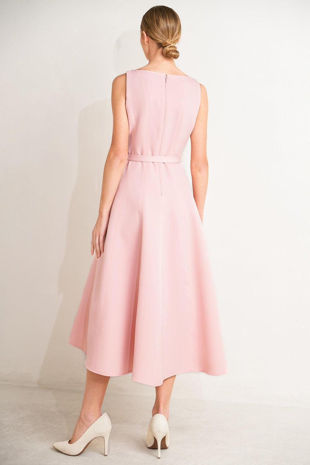 Woman wearing a beige sleeveless dress with a belt on a white background