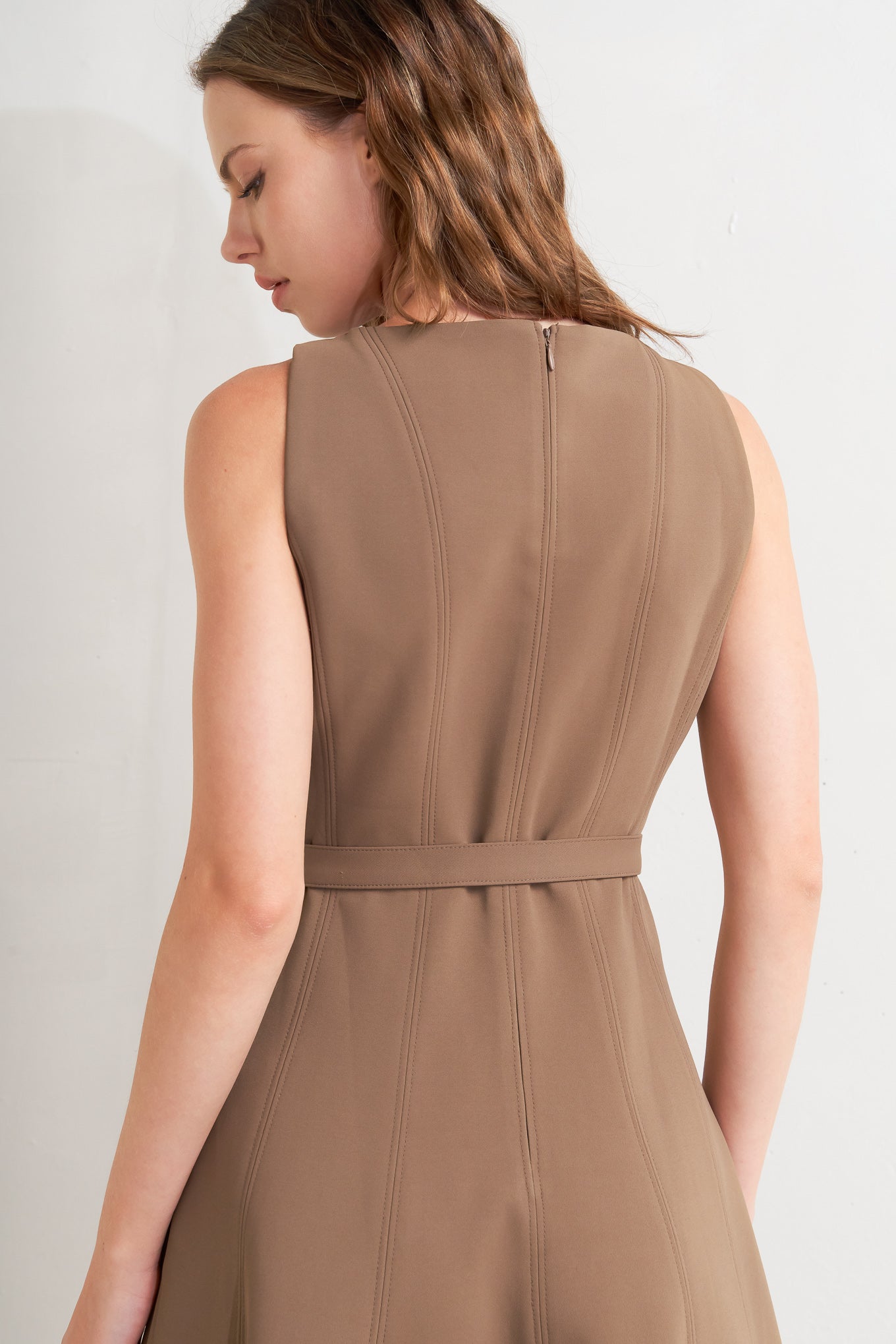 A solid woven midi dress featuring boat neckline, sleeveless, full skirt, self belt, side pocket and full skirt