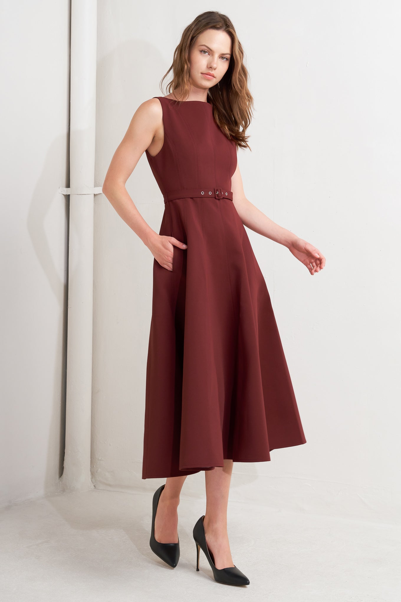 A solid woven midi dress featuring boat neckline, sleeveless, full skirt, self belt, side pocket and full skirt