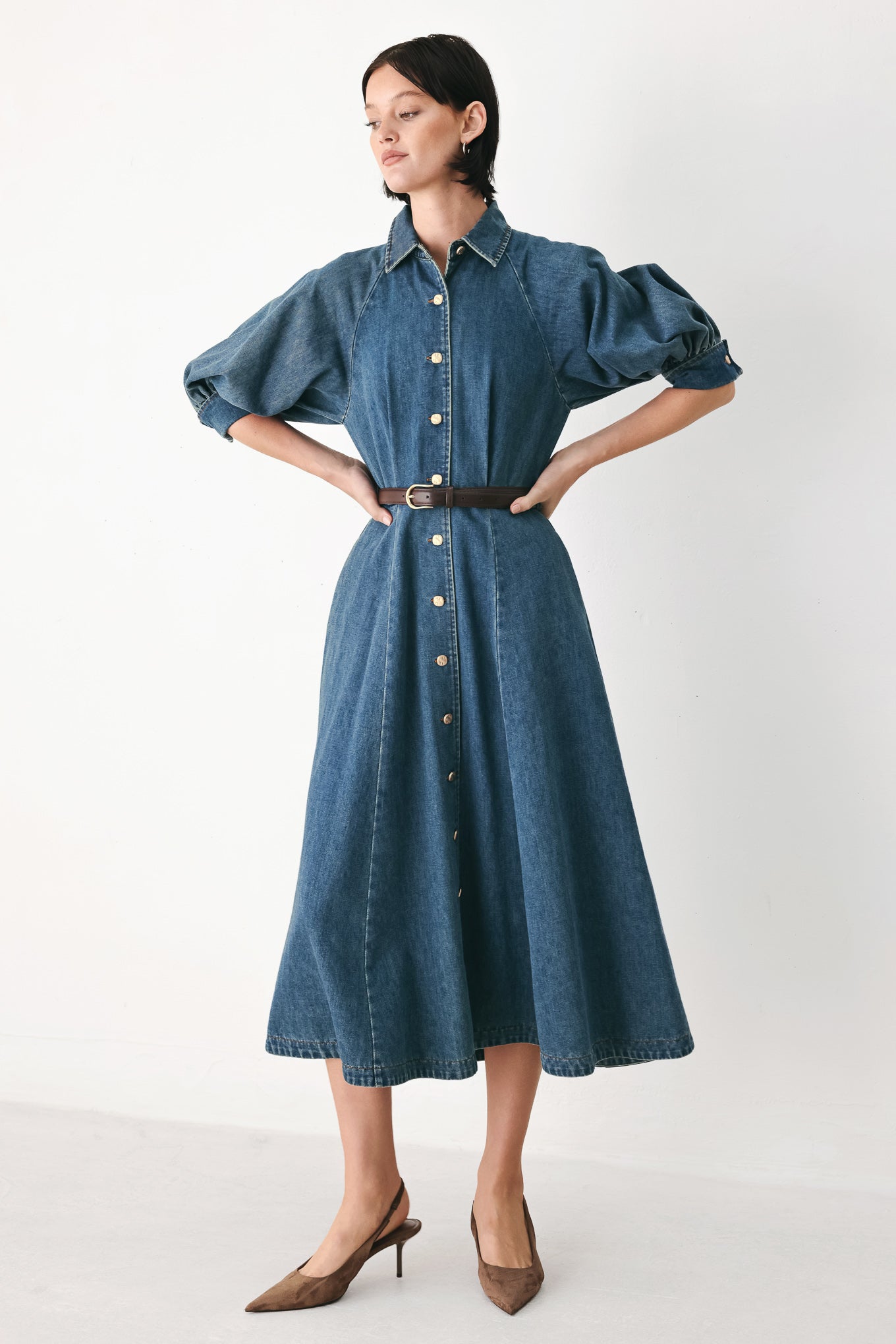 Woman wearing a blue denim dress with a belt on a beige background