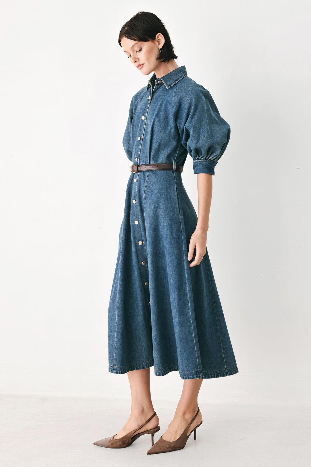 Woman wearing a blue denim dress with a belt on a beige background