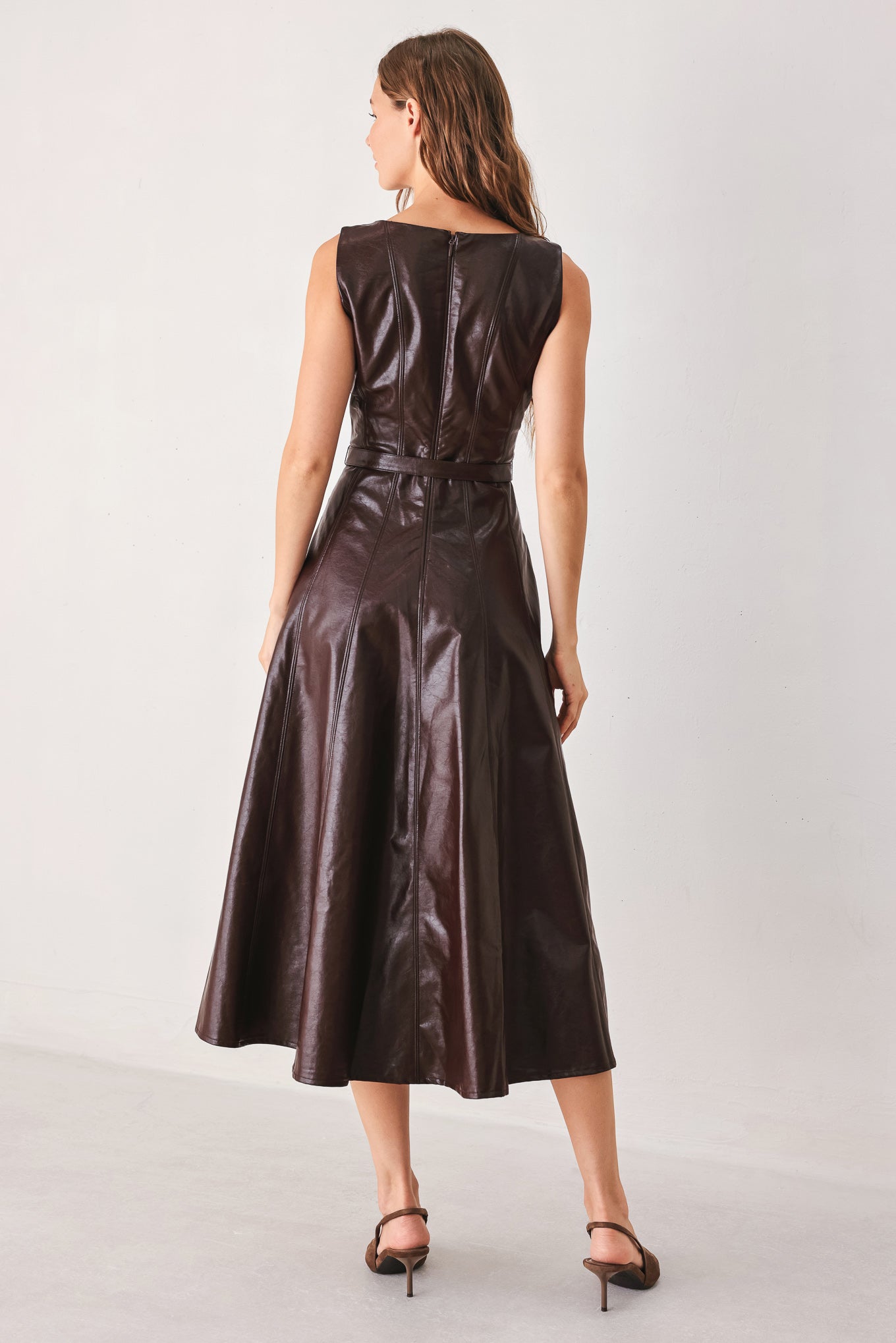 A woman wearing a sleeveless, dark brown faux-leather midi dress with a defined waist belt and a flared skirt | FREEMARKET