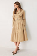 A woman models a beige double-breasted trench coat with a matching waist belt, paired with brown pointed-toe heels | FREEMARKET