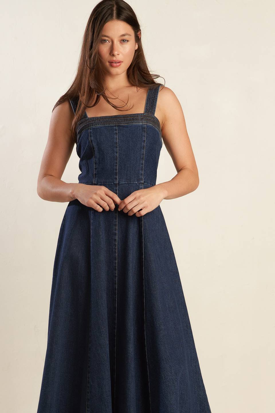 A dark washed denim midi dress featuring straight neckline, wide strap, full skirt and back zipper closure.