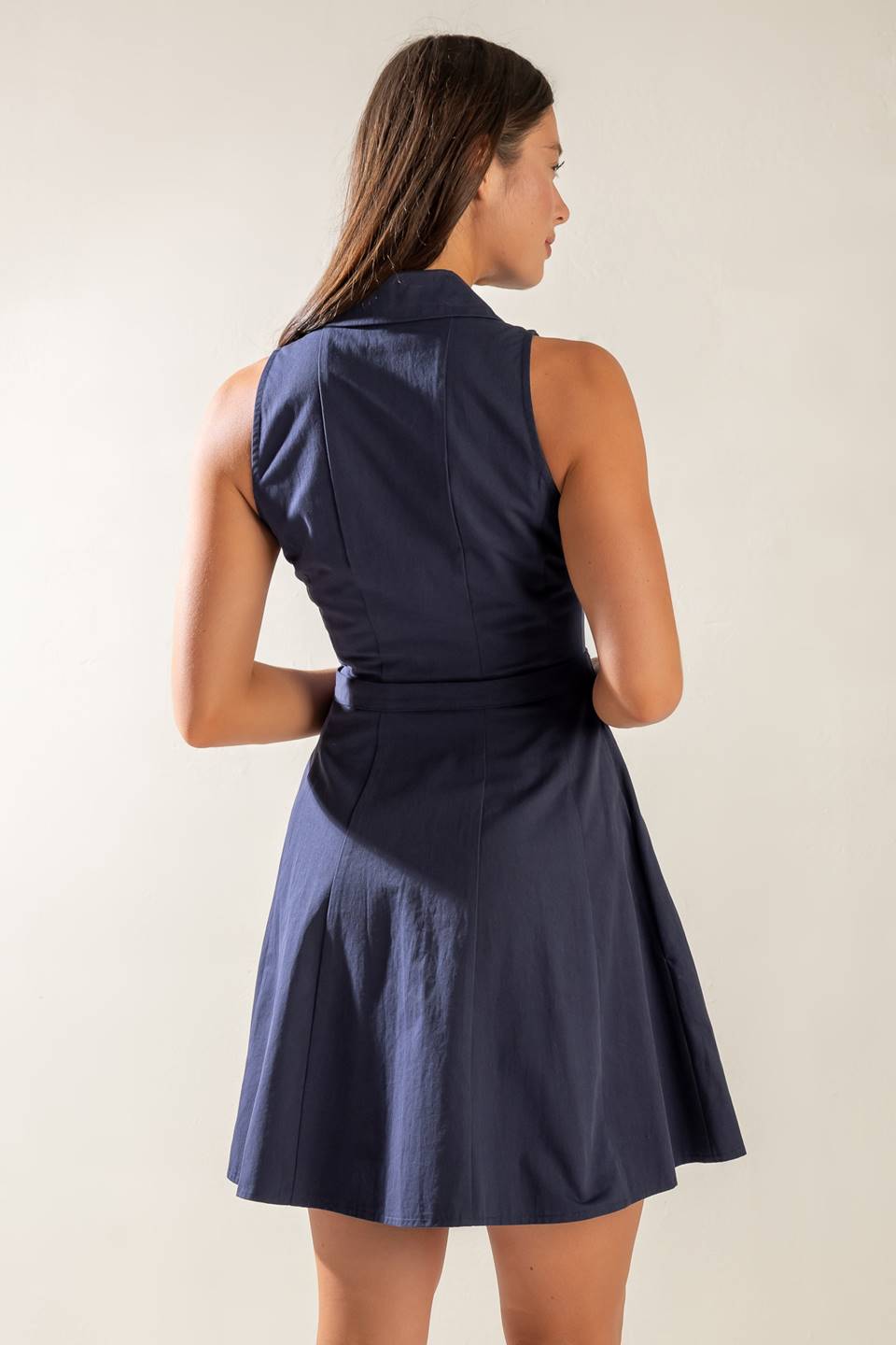 A sleeveless, solid navy woven mini dress featuring collar, button down, self belt and full skirt.