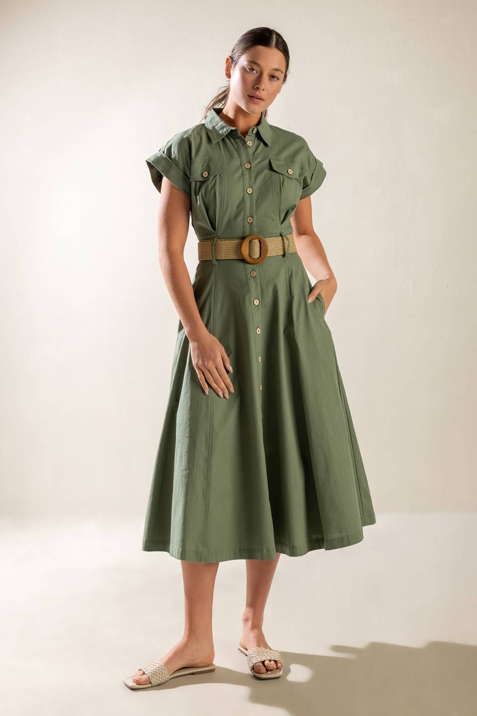 A solid olive woven midi dress featuring collar, short cuffed sleeve, button down, contrasting belt, side pockets and full skirt.