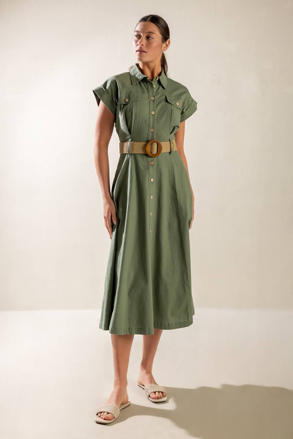 A solid olive woven midi dress featuring collar, short cuffed sleeve, button down, contrasting belt, side pockets and full skirt.