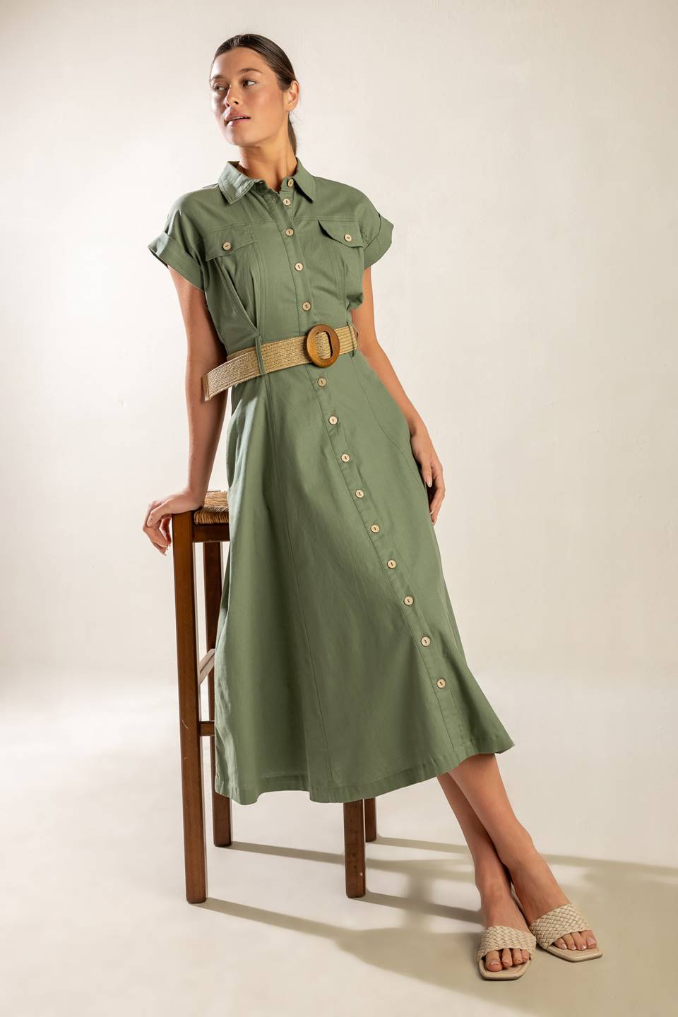 A solid olive woven midi dress featuring collar, short cuffed sleeve, button down, contrasting belt, side pockets and full skirt.