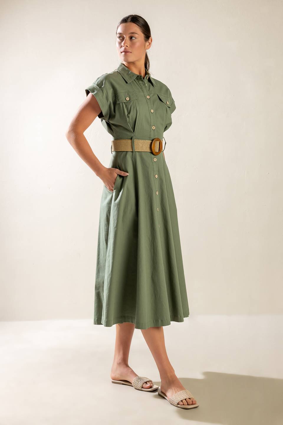 A solid olive woven midi dress featuring collar, short cuffed sleeve, button down, contrasting belt, side pockets and full skirt.