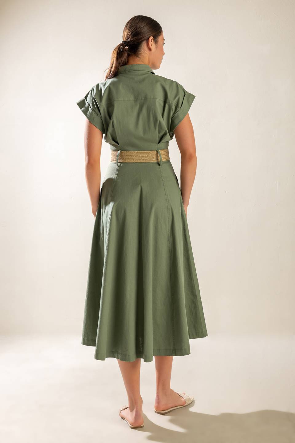 A solid olive woven midi dress featuring collar, short cuffed sleeve, button down, contrasting belt, side pockets and full skirt.