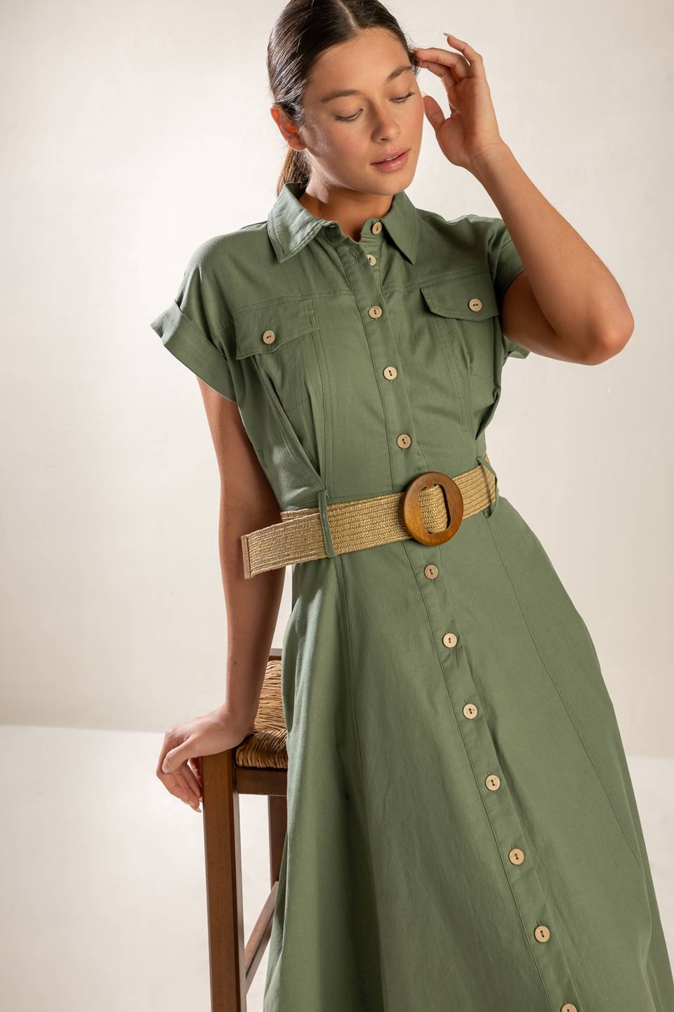 A solid olive woven midi dress featuring collar, short cuffed sleeve, button down, contrasting belt, side pockets and full skirt.