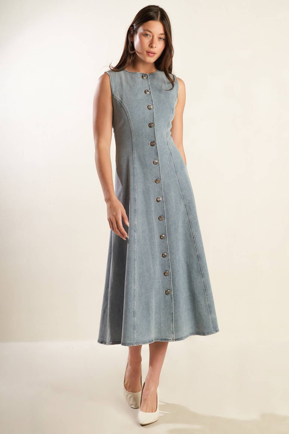 A sleeveless, washed light denim midi dress featuring round neckline, button down, self sash tie, side pockets and full skirt.