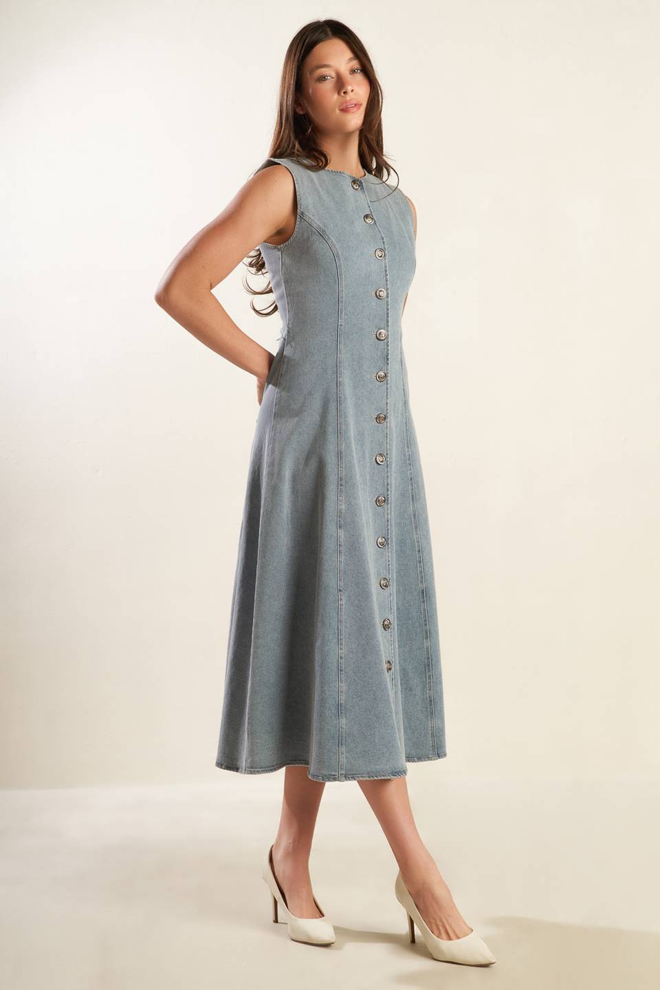 A sleeveless, washed light denim midi dress featuring round neckline, button down, self sash tie, side pockets and full skirt.