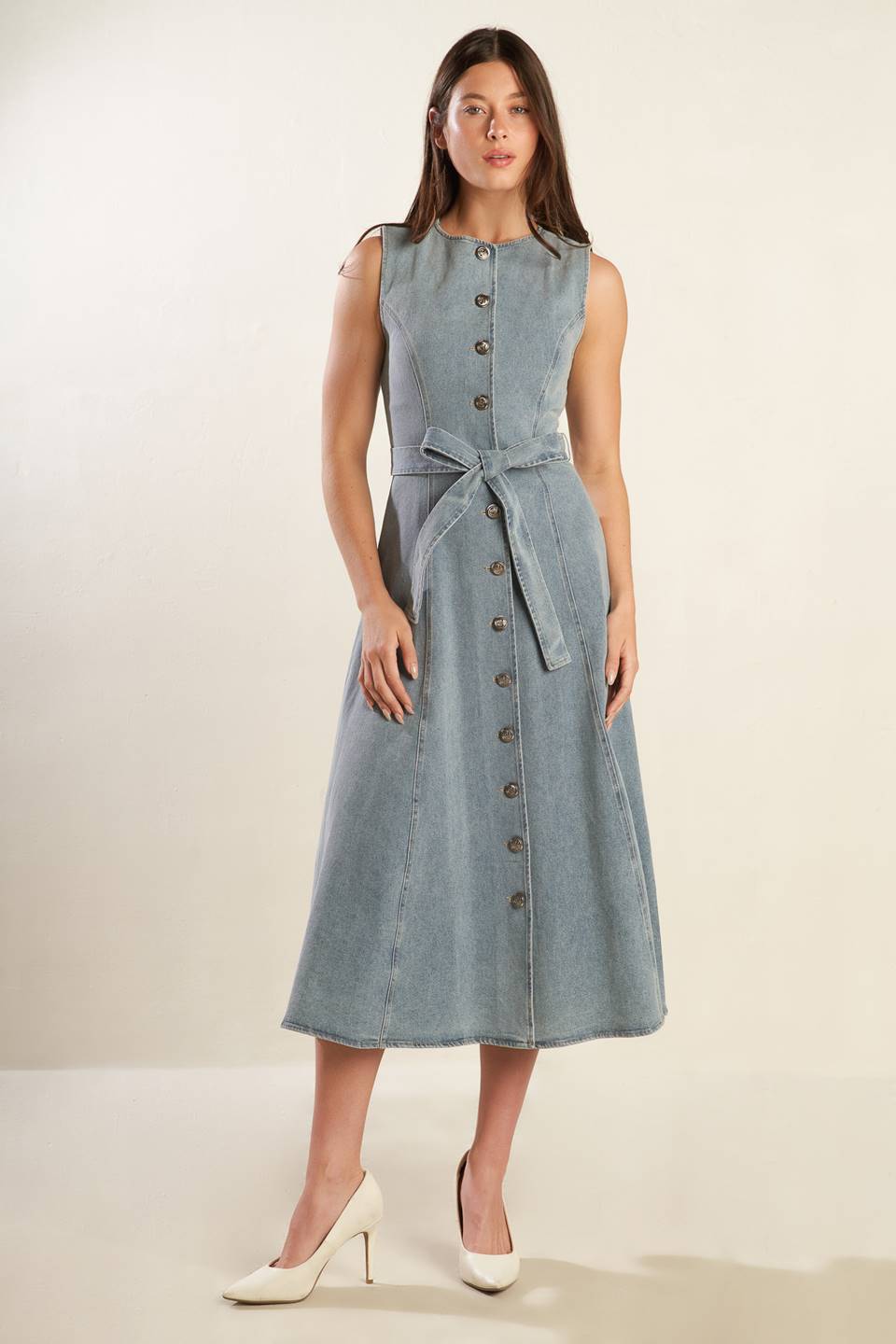 A sleeveless, washed light denim midi dress featuring round neckline, button down, self sash tie, side pockets and full skirt.