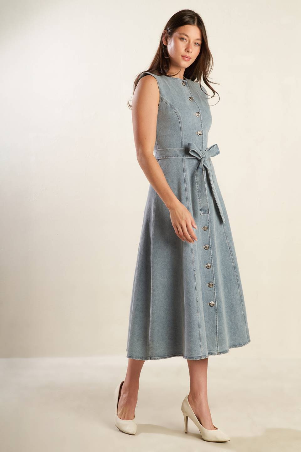 A sleeveless, washed light denim midi dress featuring round neckline, button down, self sash tie, side pockets and full skirt.