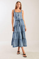 A washed denim dress featuring straight neckline, straps, front zipper closure, self sash tie and tiered skirt.