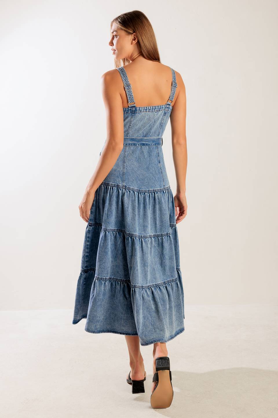 A washed denim dress featuring straight neckline, straps, front zipper closure, self sash tie and tiered skirt.