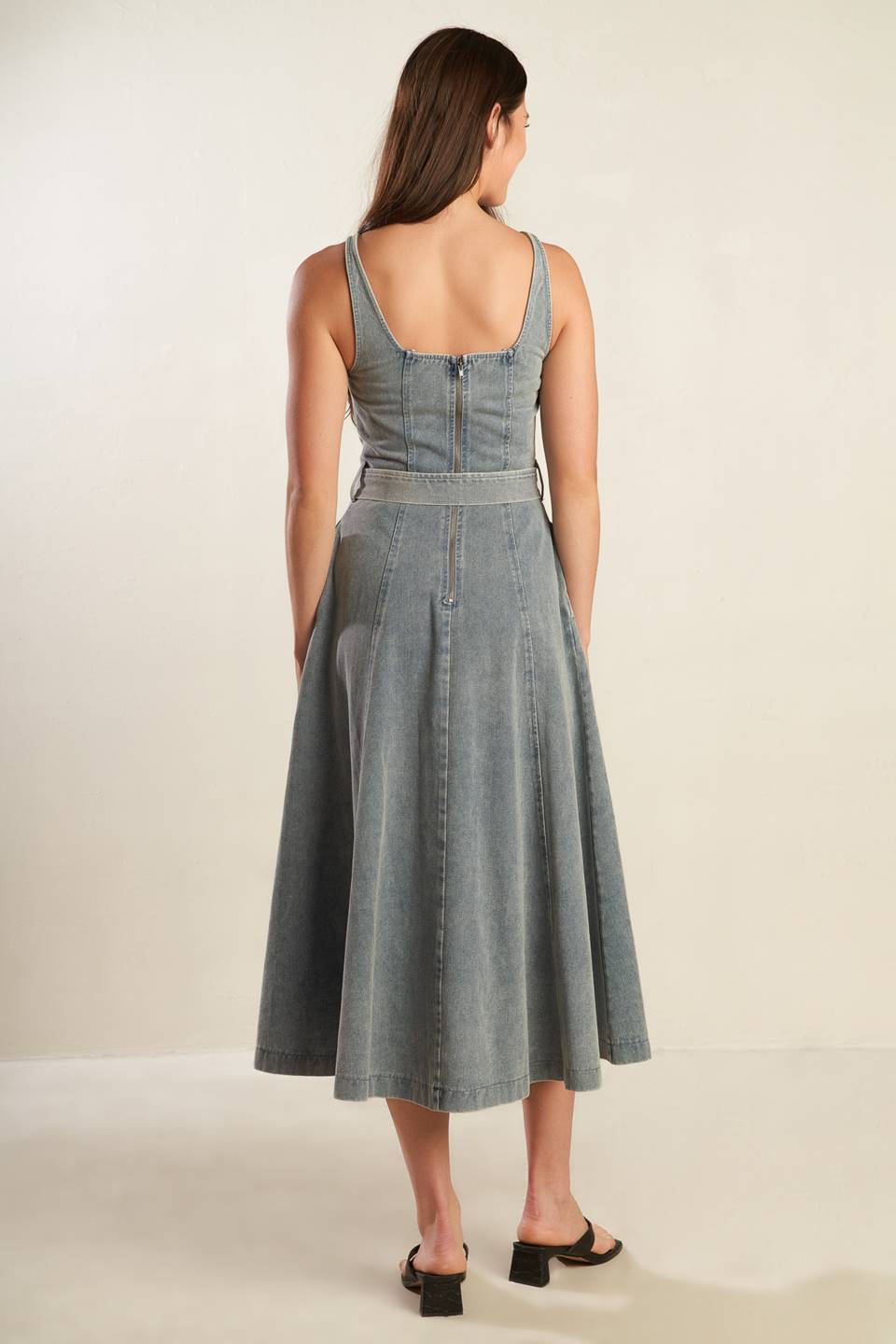 A washed denim midi dress featuring straight neckline, straps, circle skirt, self sash tie and back zipper closure.