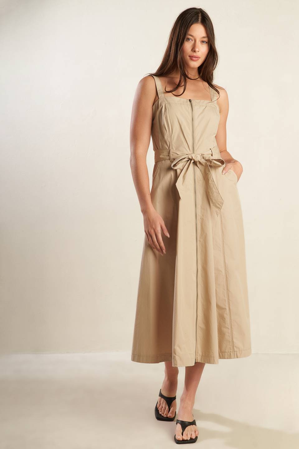 A solid woven midi dress featuring straight neckline, straps, self belt, front zipper closure and full skirt.