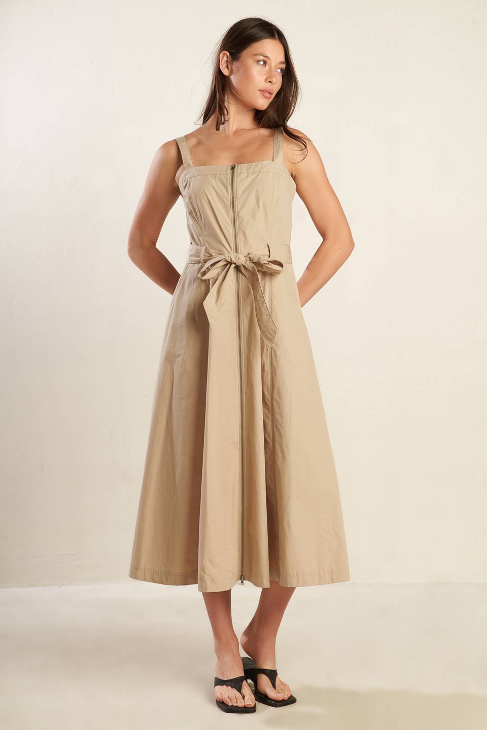 A solid woven midi dress featuring straight neckline, straps, self belt, front zipper closure and full skirt.