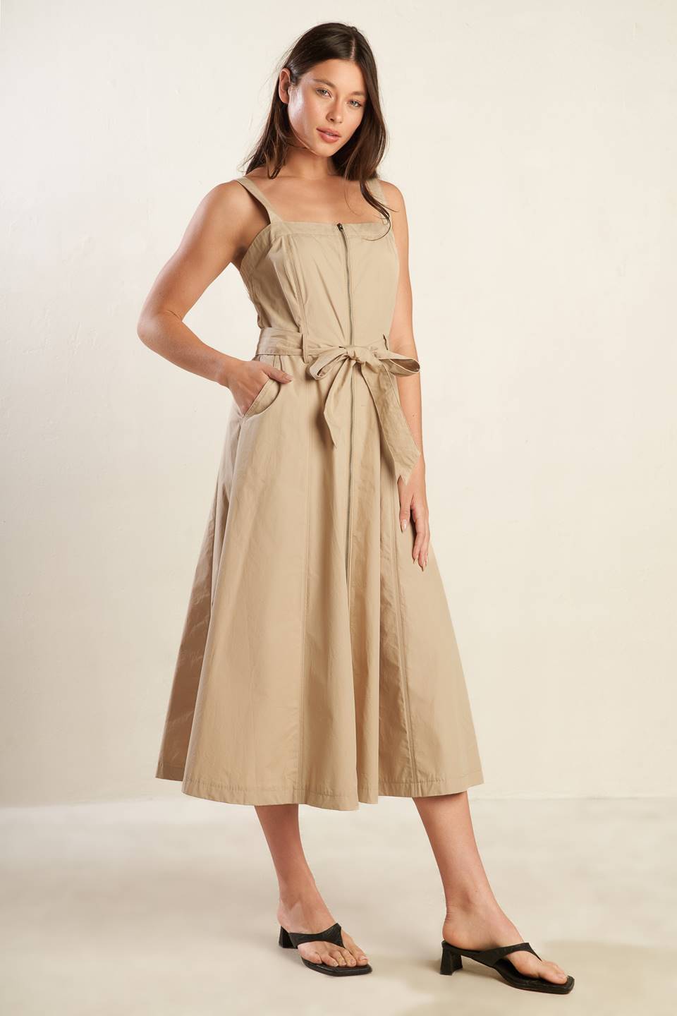 A solid woven midi dress featuring straight neckline, straps, self belt, front zipper closure and full skirt.