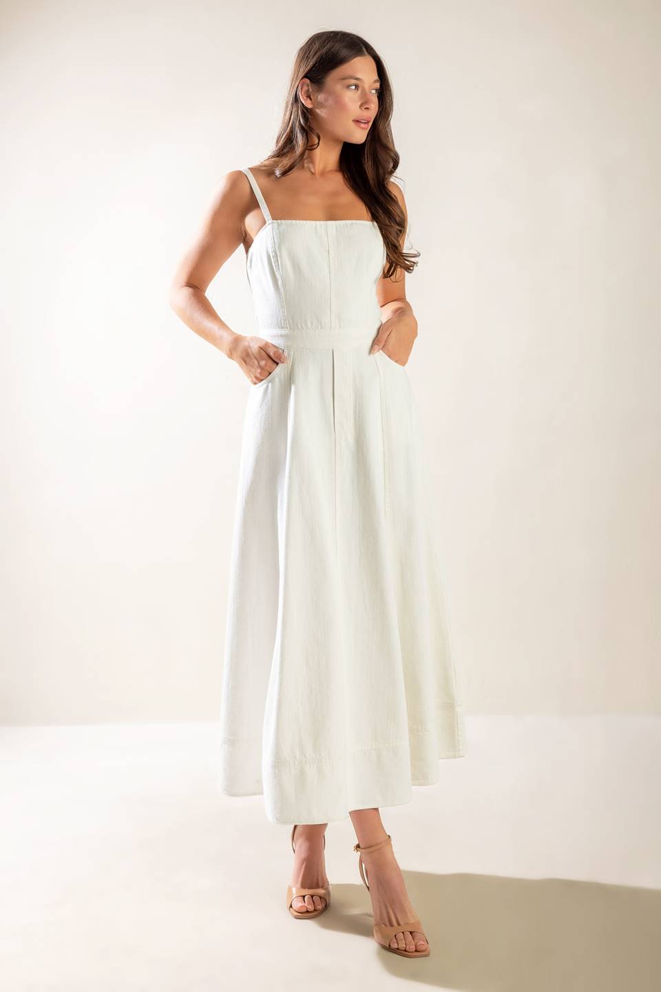 A solid white woven midi dress featuring straight neckline, straps, side pockets, circle skirt, bare back with tie and zipper closure.