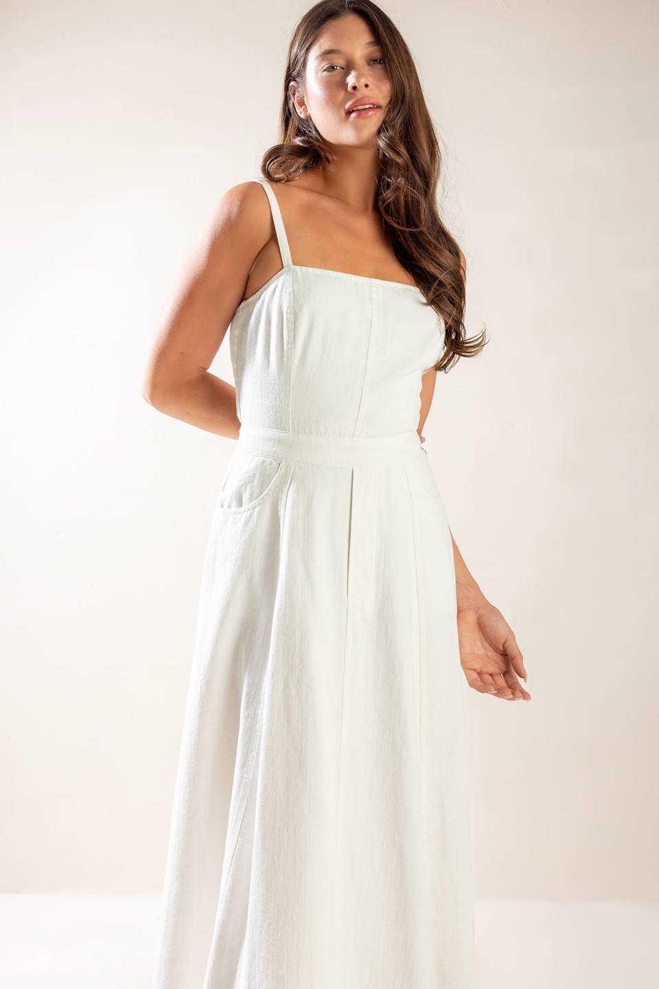 A solid white woven midi dress featuring straight neckline, straps, side pockets, circle skirt, bare back with tie and zipper closure.