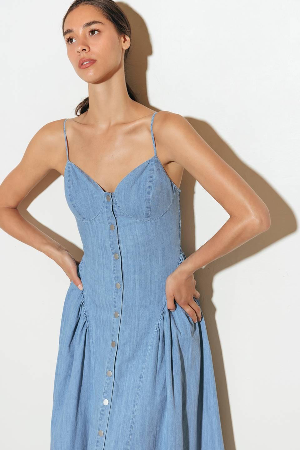 A solid lightweight denim midi dress featuring cami top, straps, button down, side shirring detail, full skirt and backside smocked detail