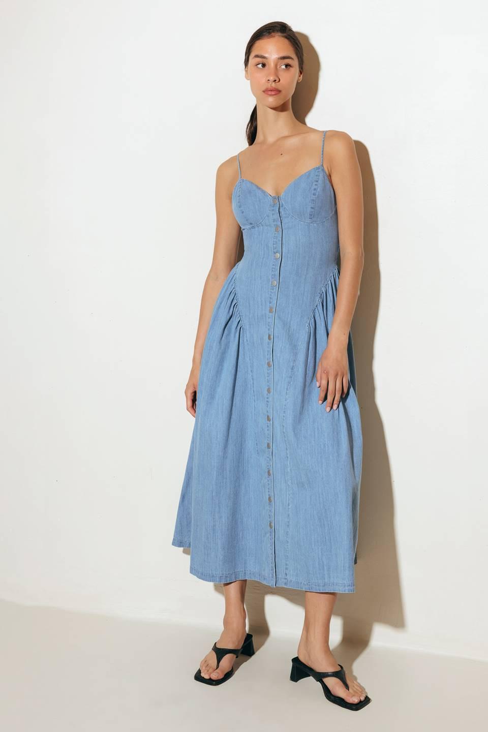 A solid lightweight denim midi dress featuring cami top, straps, button down, side shirring detail, full skirt and backside smocked detail