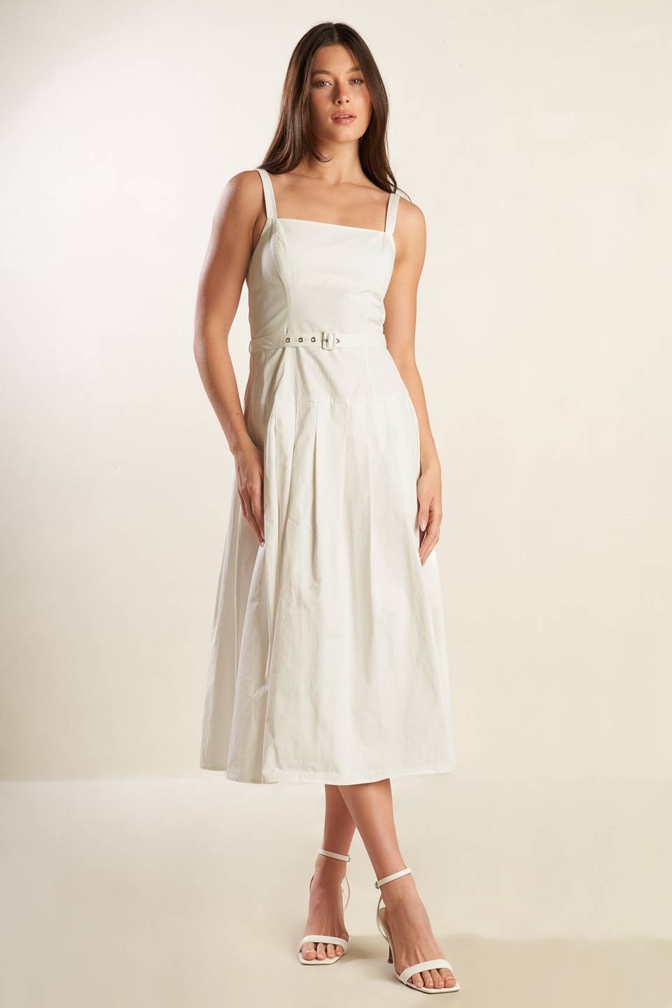 A solid white woven midi dress featuring straight neckline, straps, drop waist, self belt, box pleat and back zipper closure.