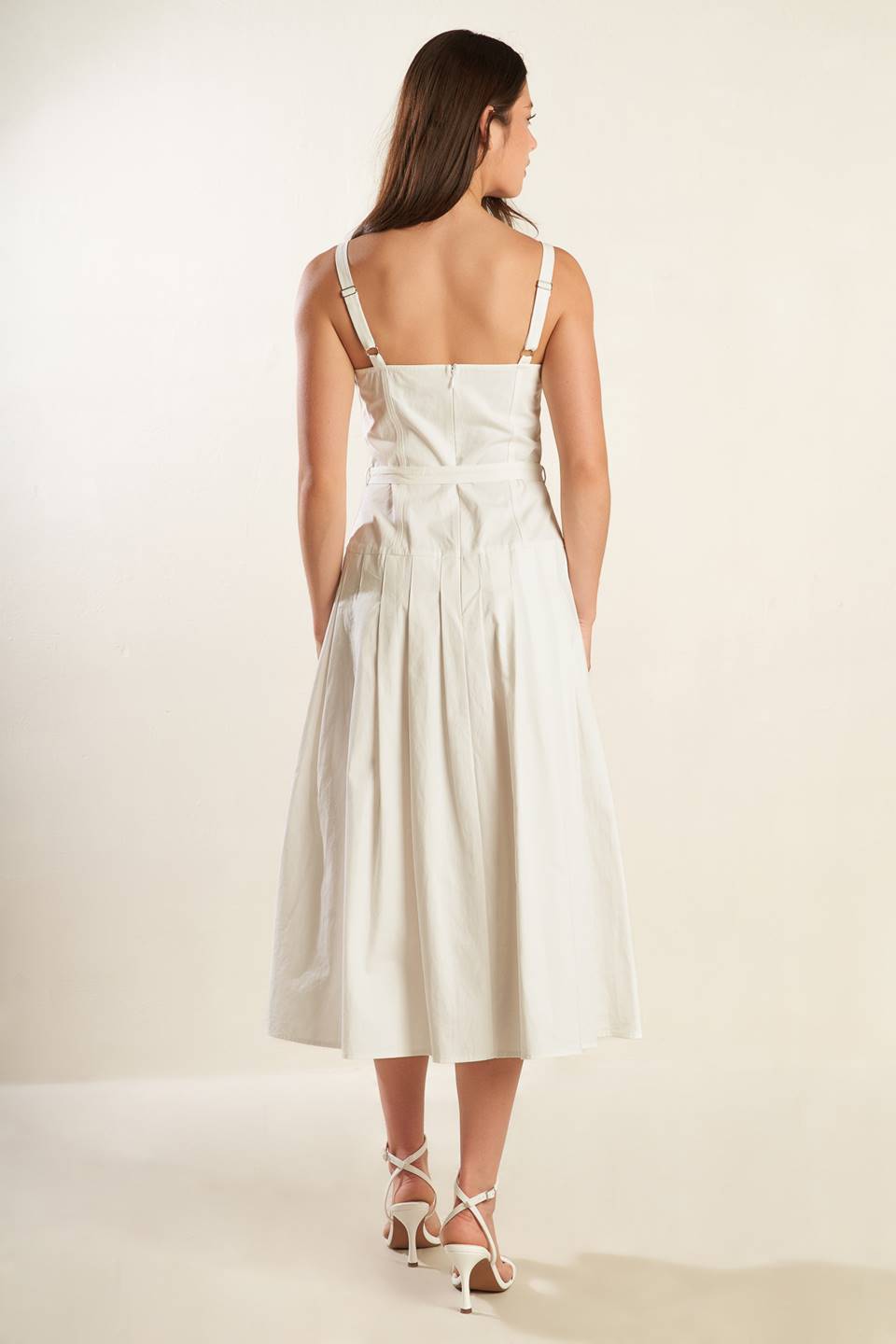 A solid white woven midi dress featuring straight neckline, straps, drop waist, self belt, box pleat and back zipper closure.