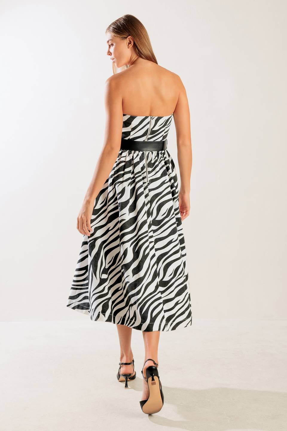 A strapless, black and white, zebra print woven midi dress featuring contrasting belt, side pockets, full skirt, and back zipper closure