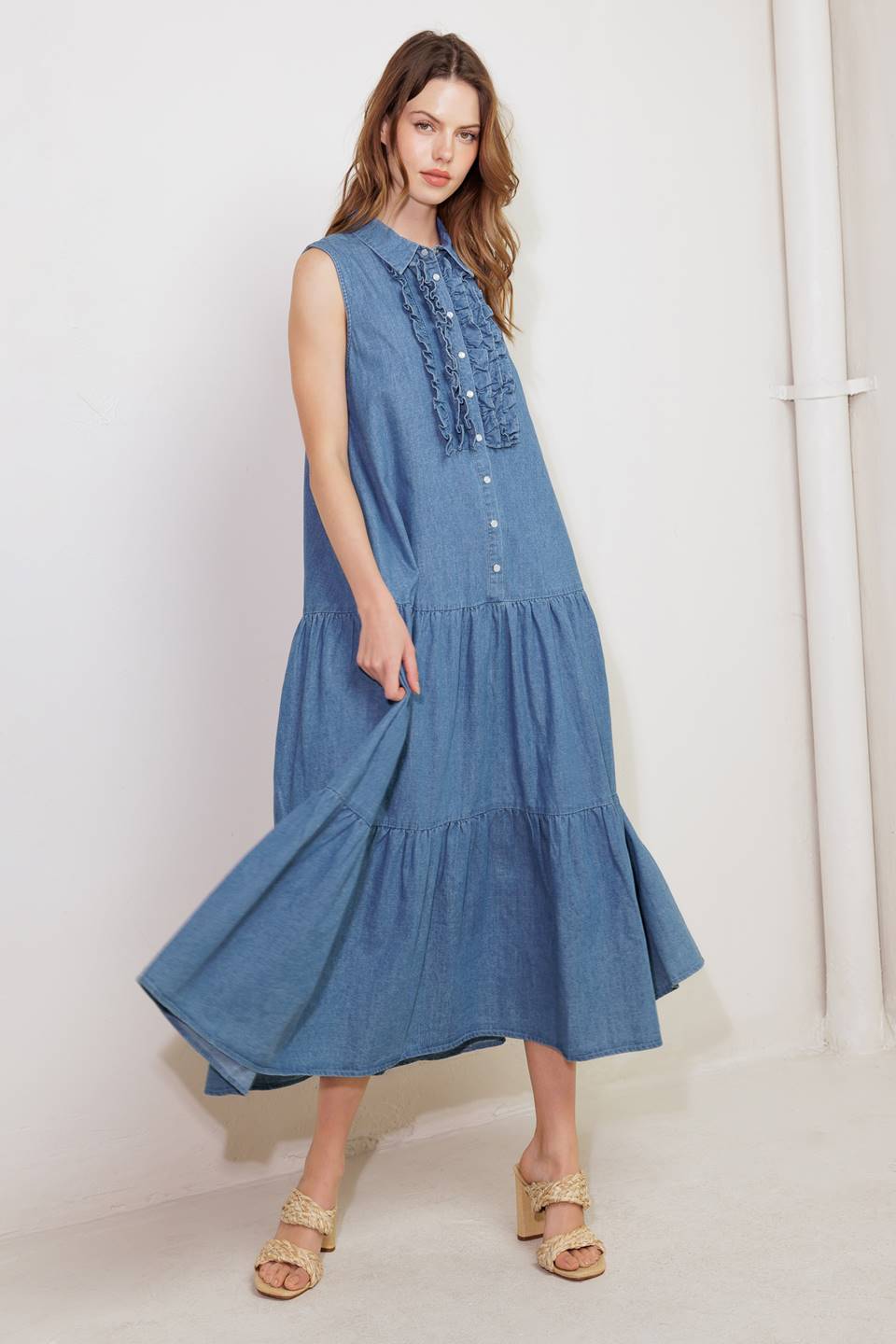 A washed denim midi dress featuring collar, snap button down, ruffled front, sleeveless, self sash tie and tiered skirt